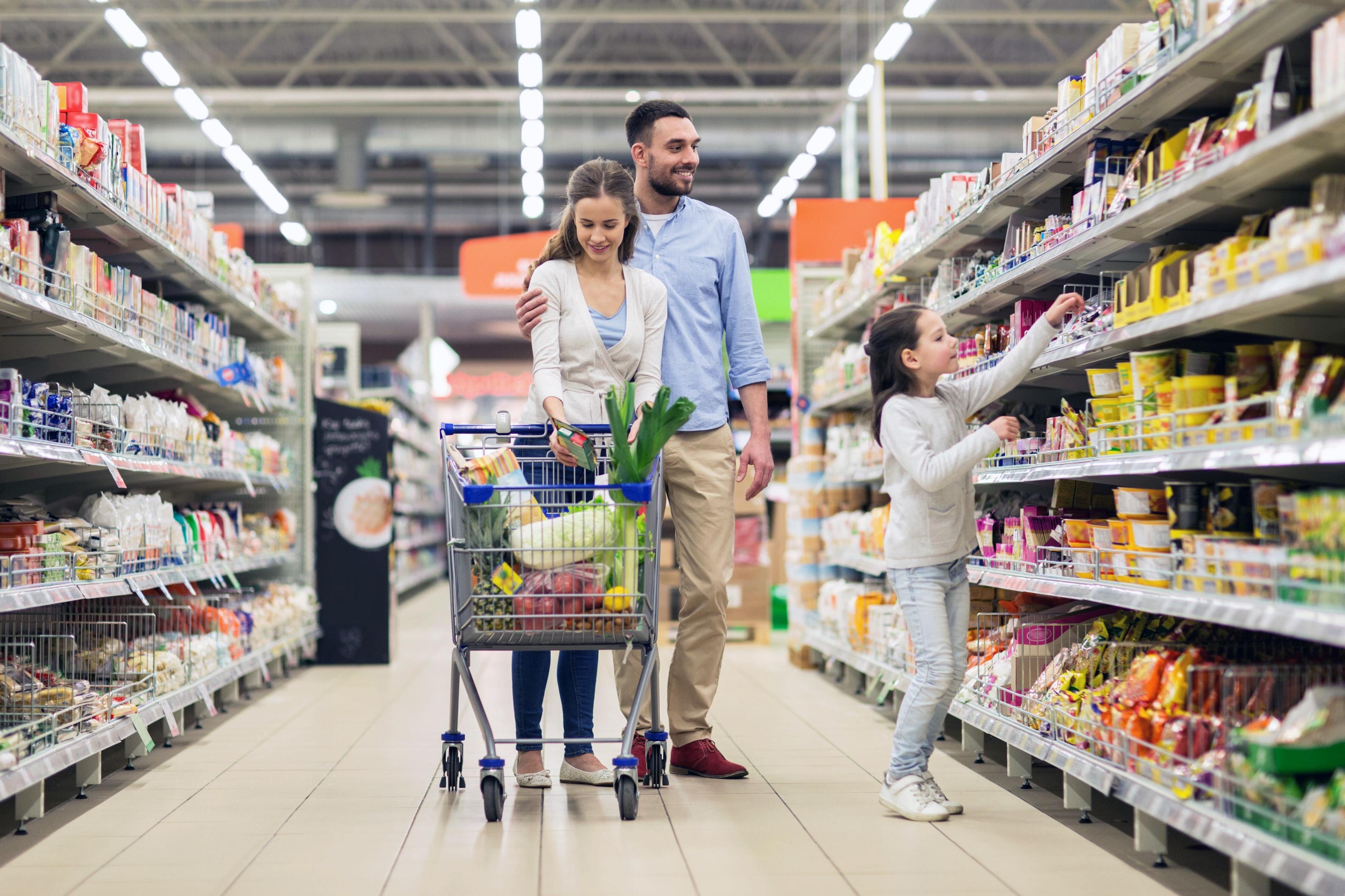 A family pushes a cart down the aisle of a grocery store.
